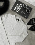 Flatlay with grey bodysuit with 'Superior' logo, black book with 'Tom Ford' text, sunglasses, and black shoes