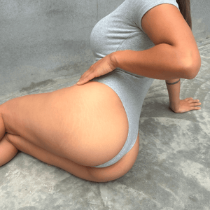 Grey short sleeve bodysuit modelling front of grey concrete on the floor showing the back