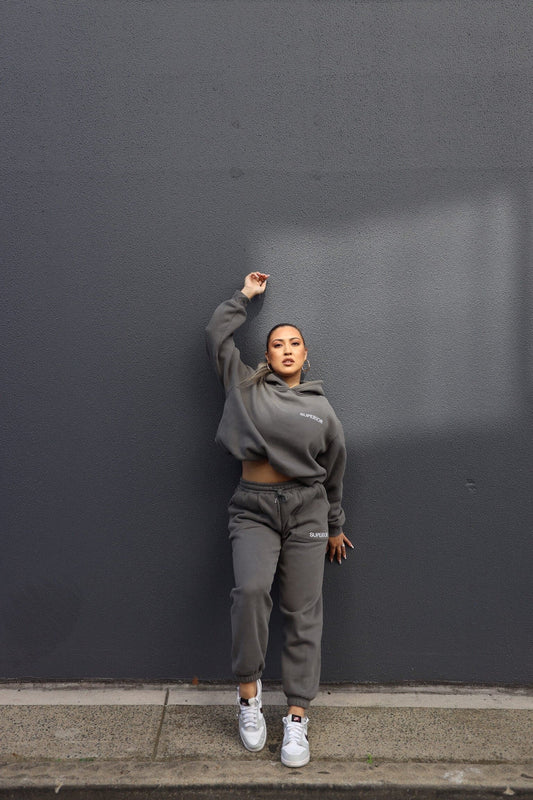 posing against charcoal wall, one arm up in the air in the full dark grey set