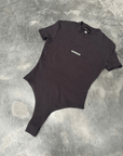 Black t-shirt short sleeve bodysuit with 'SUPERIOR' logo on a textured gray surface front on in flat lay position 