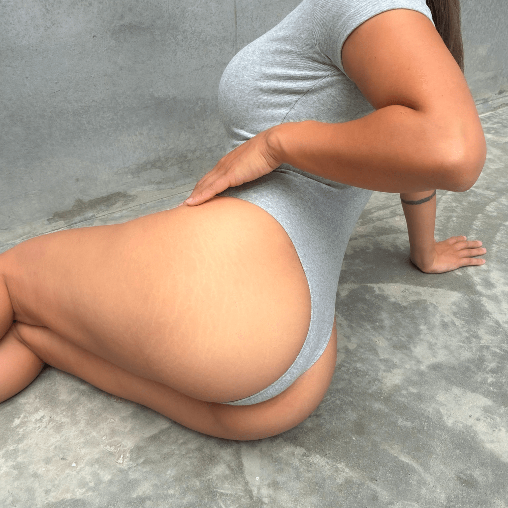 Grey short sleeve bodysuit modelling front of grey concrete on the floor showing the back 